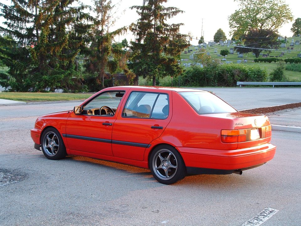 Red 1994 Volkswagen Jetta sedan with aftermarket wheels, viewed from the rear three-quarter angle