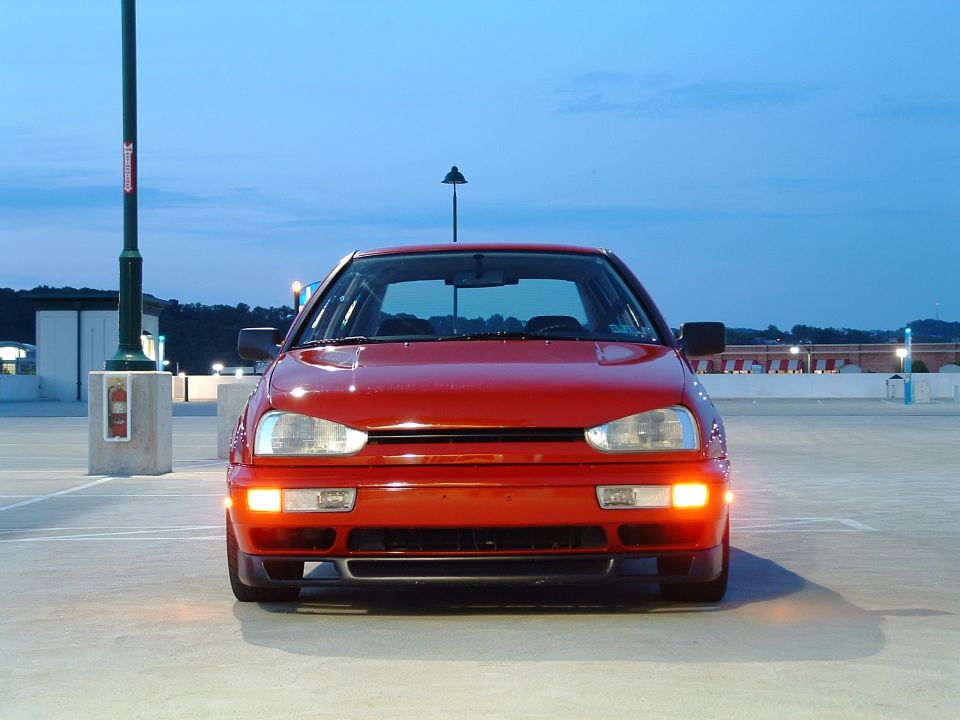 Red Volkswagen Golf Mk3 parked in a lot at dusk. The car is facing the camera