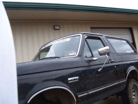 1988 Ford Bronco - A black 1988 Ford Bronco is shown from the front quarter angle, with the 'BRONCO' badge clearly visible on the fender.