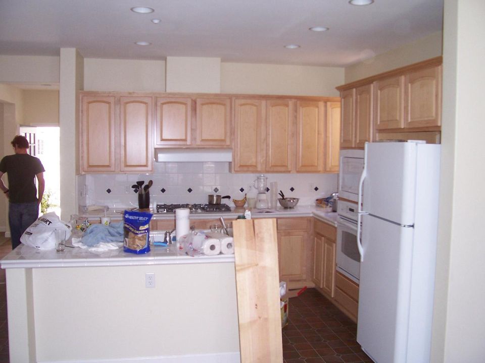 Kitchen mid-remodel with unfinished maple cabinets, white appliances and a person standing near the island