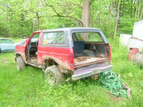 1984 Ford Bronco - This red Ford Bronco appears to be in disrepair, with its doors removed and body panels showing significant damage.