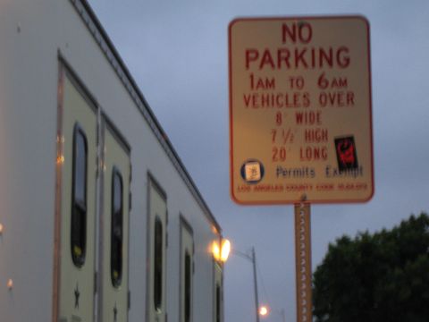 1990 Ford Bronco - red-and-white No Parking sign for oversized vehicles stands beside a parked white trailer under a twilight sky.