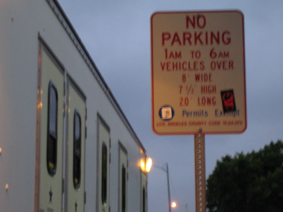 Orange No Parking sign for oversized vehicles beside a white trailer at twilight