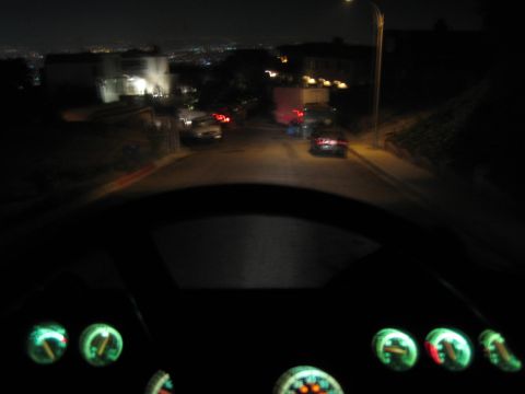 1990 Ford Bronco - From behind the wheel at night, illuminated gauges glow as a hillside residential street and distant city lights stretch ahead.