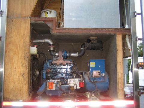 1990 Ford Bronco - blue diesel engine and generator sit inside the open plywood-lined compartment of a support trailer.