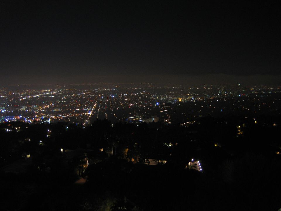Wide nighttime view of a sprawling illuminated city grid seen from the hills
