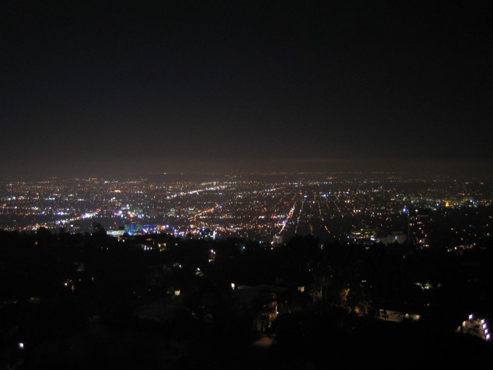 Nighttime panorama of a glittering city grid below dark hillside foreground