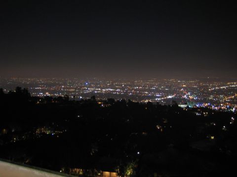 1990 Ford Bronco - sea of distant city lights glows softly under a hazy night sky, seen from a darkened hilltop.