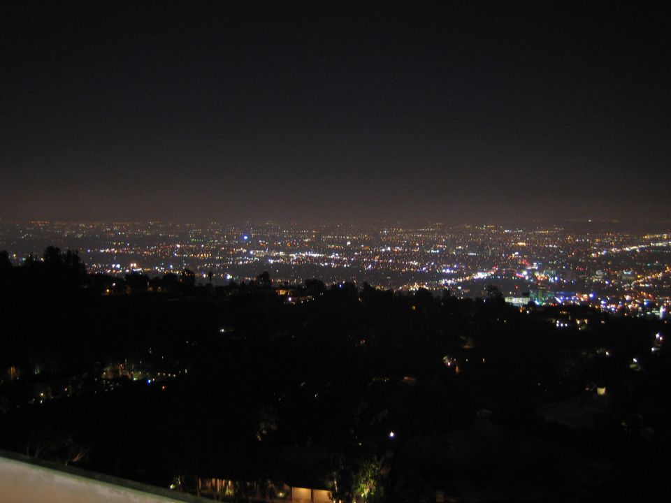 Distant city lights glowing at night beneath a dark sky from a hilltop vantage