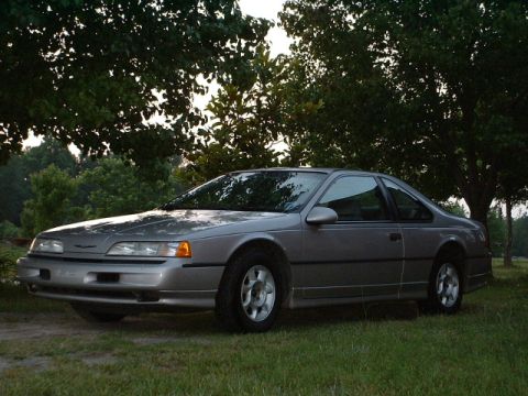 1989 Ford Thunderbird - A 1989 Ford Thunderbird coupe is shown parked outdoors in front of trees.