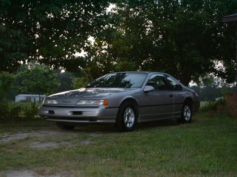 1989 Ford Thunderbird - A 1989 Ford Thunderbird coupe is parked on a grassy area with trees in the background.