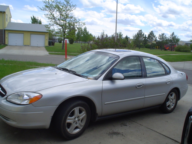 Silver four-door sedan parked on driveway, front three-quarter view, near yellow garage.