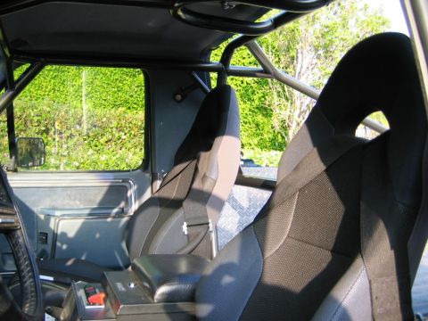 1985 Ford Bronco - The interior of a vehicle is shown, equipped with a roll cage and racing seats.