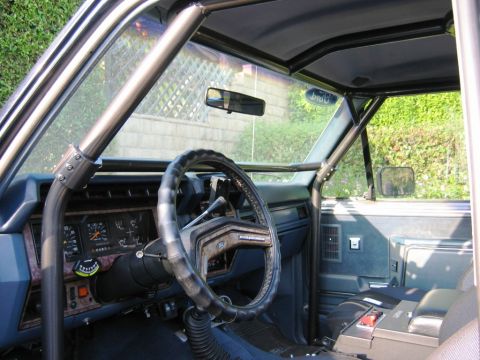 1985 Ford Bronco - The interior of this vehicle features a custom roll cage, a worn steering wheel, and a dashboard with various gauges.