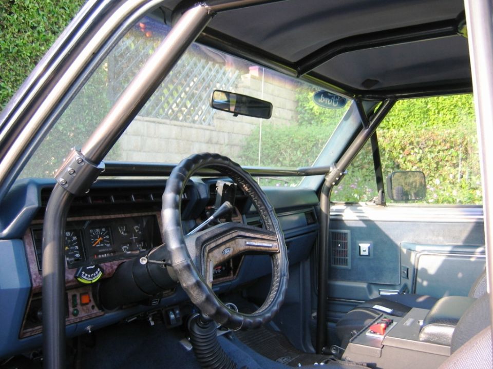 Ford Bronco interior with wrapped steering wheel, gauges, woodgrain dash, and roll cage bar
