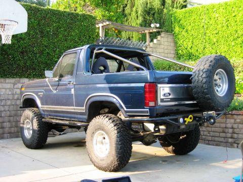 1985 Ford Bronco - This modified 1985 Ford Bronco features a prominent roll cage and a rear-mounted spare tire, viewed from the back.