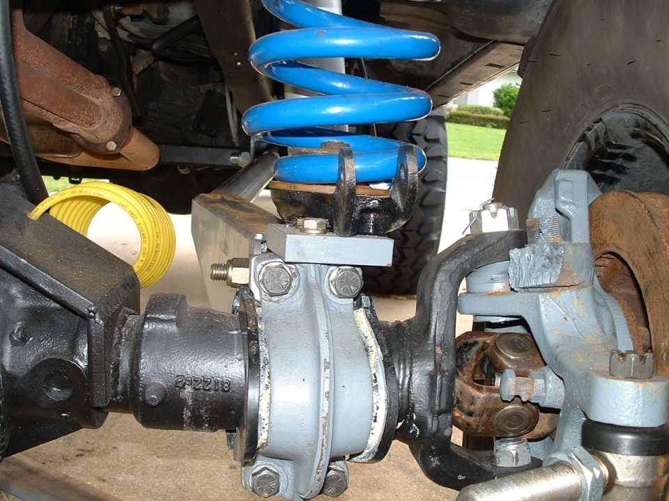 Front axle assembly with gray-painted housing, blue coil spring, and U-joint under a vehicle