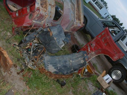 1987 Ford F-150 - Scattered red vehicle parts and engine components lie on the grass near a gray pickup truck.