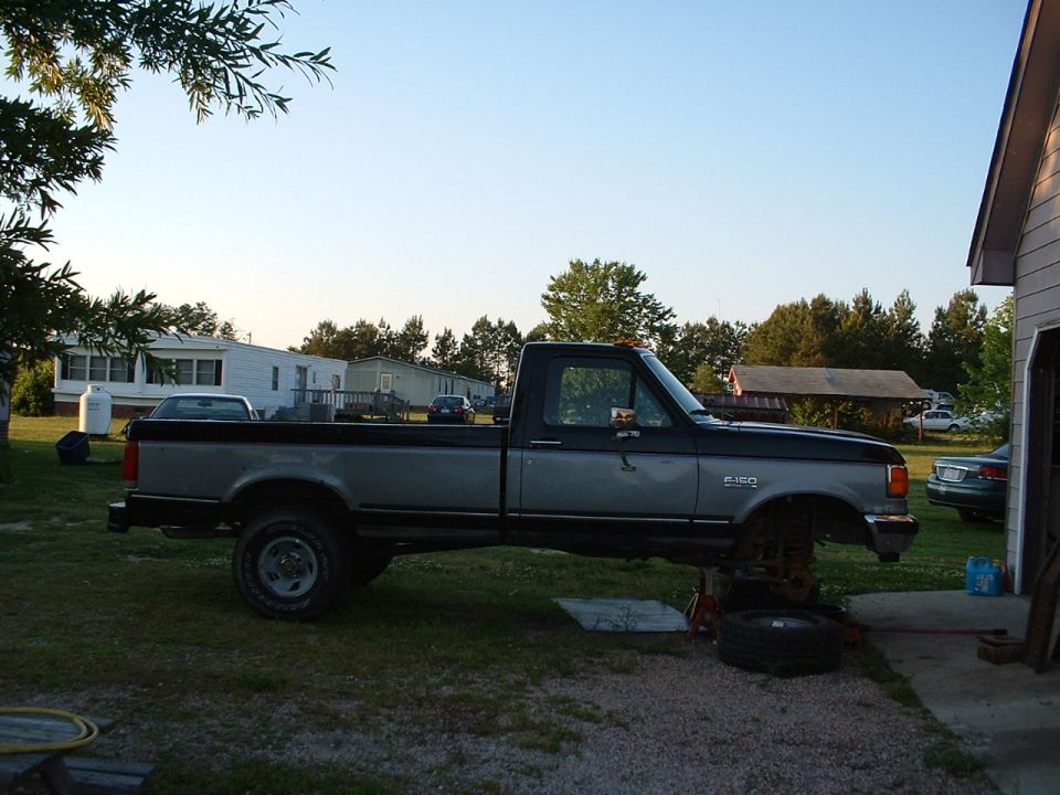 Two-tone Ford F-250 regular cab pickup parked on rural lawn, rear wheel off