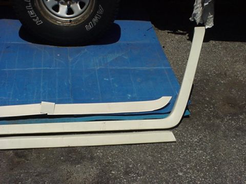 1989 Ford Bronco - Several white trim pieces are arranged on a blue mat, with a vehicle tire visible in the upper left corner.