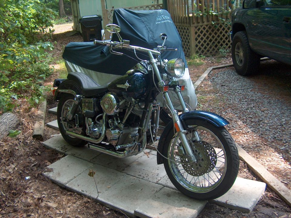 Blue chrome Harley cruiser parked on pavers with green truck beside it