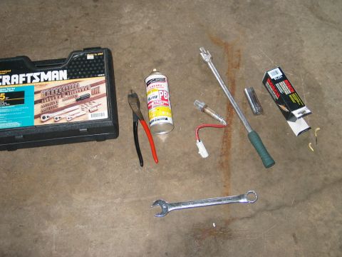 1995 Ford Bronco - Tools and engine parts, including an oxygen sensor, socket set, and wrenches, laid out on a concrete surface.