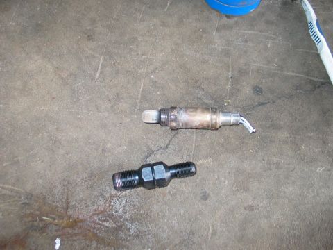 1995 Ford Bronco - Two automotive parts, an oxygen sensor and a bolt, lie on a rough concrete surface.