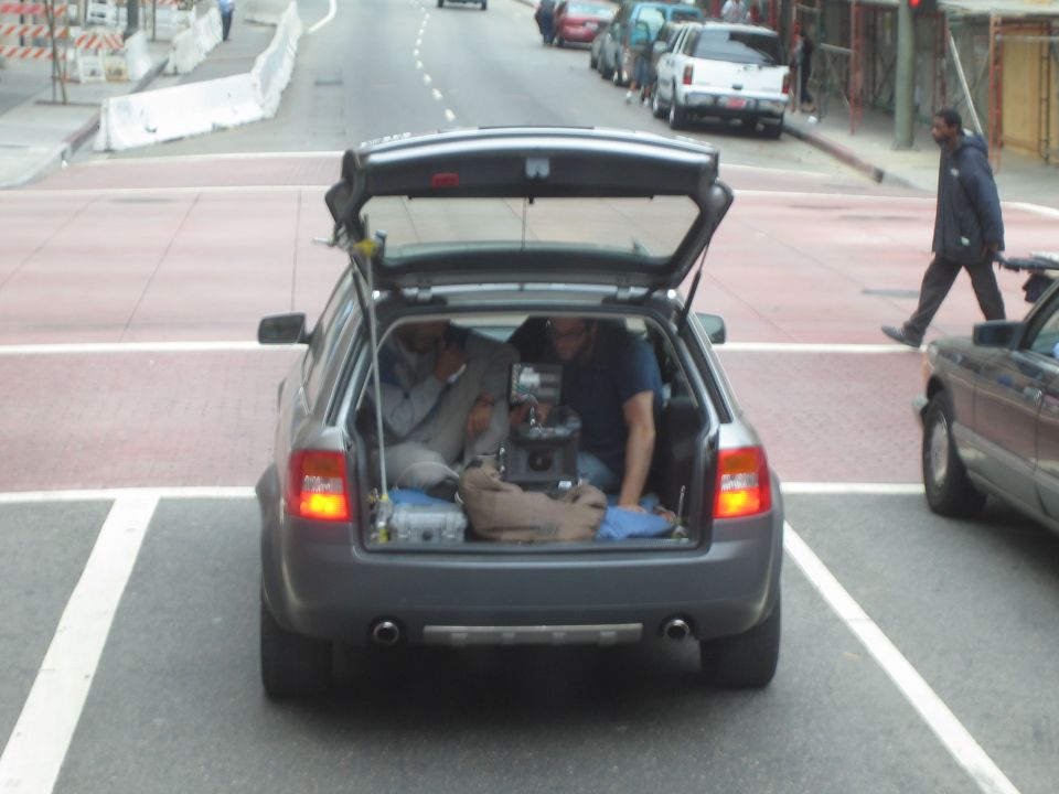 Gray station wagon with open rear hatch holding camera gear, parked on a city street