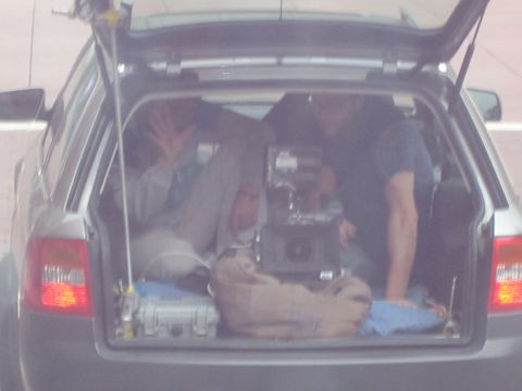 1990 Ford Bronco - View into the open rear hatch of a gray wagon packed with a large film camera, cases and a person waving inside.