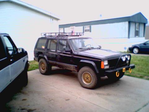 1995 Ford Bronco - A black SUV with a roof rack and aftermarket bumper is parked next to another vehicle.