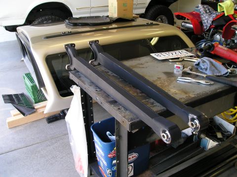 1993 Ford Bronco - Extended radius arms are laid out on a workbench, with parts of a 1993 Ford Bronco visible in the background.