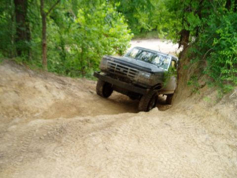 1990 Ford Bronco - This 1990 Ford Bronco tackles a challenging sandy trail surrounded by lush green trees.