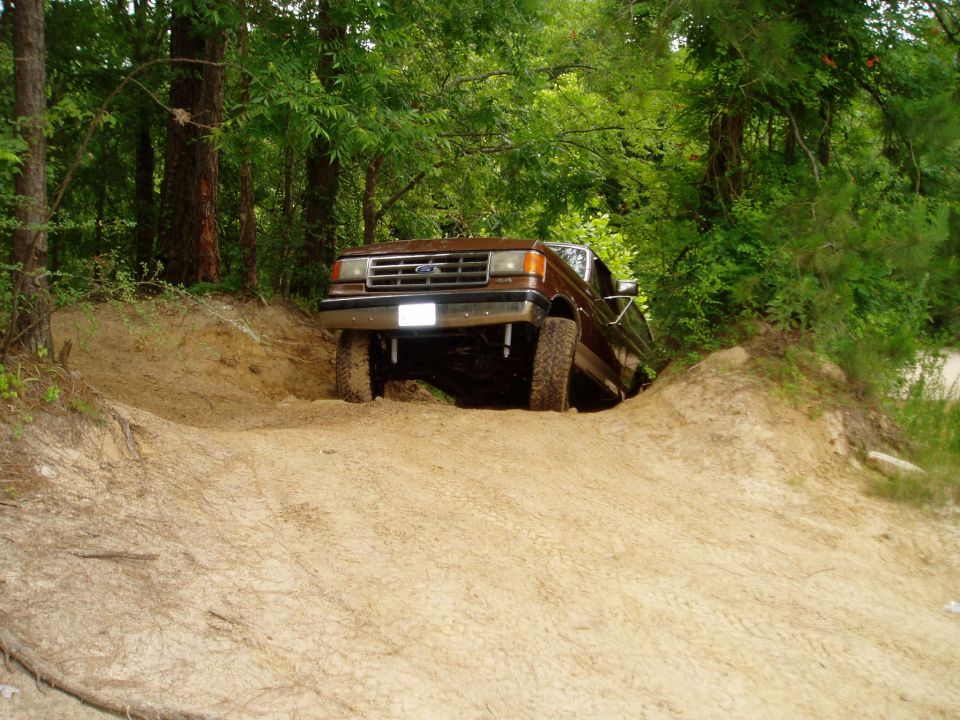 1990 Ford Bronco climbing a steep dirt embankment in a wooded area