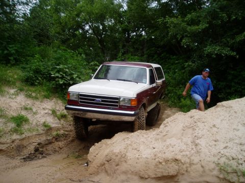 1990 Ford Bronco - A Ford Bronco navigates a sandy trail with a man walking nearby.