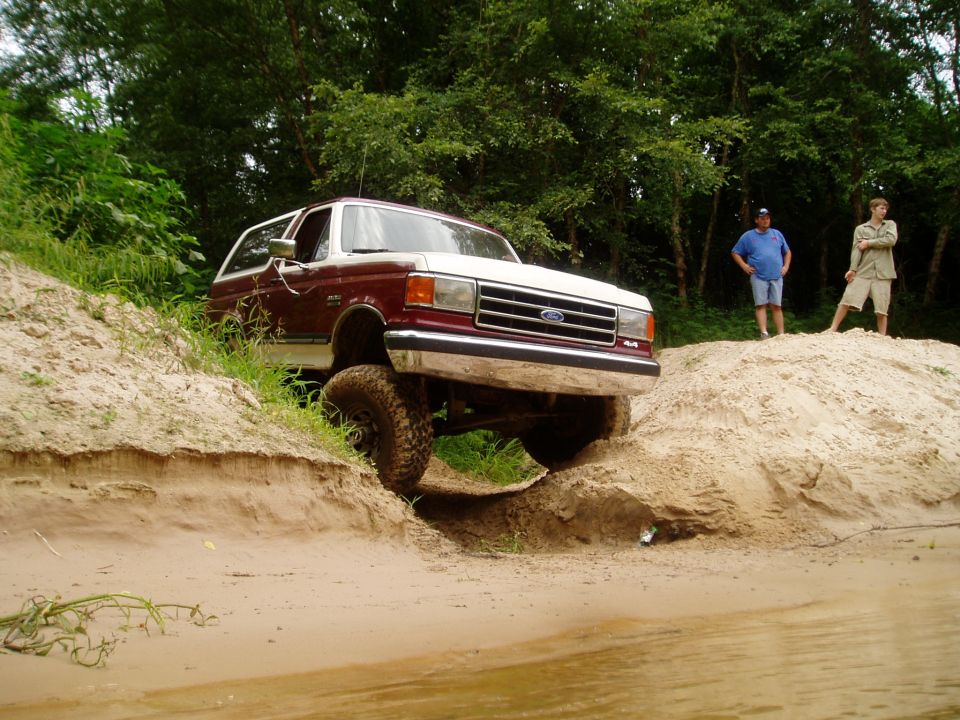 1990 Ford Bronco climbing a sand dune with two people watching