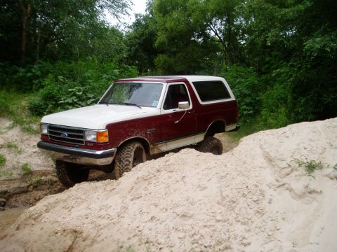 1990 Ford Bronco - This Ford Bronco is navigating a challenging off-road course with sandy and muddy terrain.