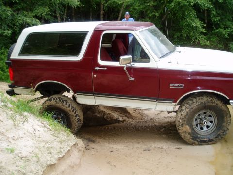 1990 Ford Bronco - A maroon and white Ford Bronco navigates a dirt trail with large off-road tires.