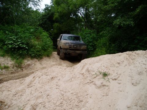 1990 Ford Bronco - A dusty Ford Bronco navigates a sandy trail through a wooded area.