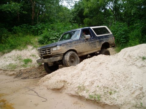 1990 Ford Bronco - A muddy Ford Bronco navigates a challenging off-road terrain with sandy inclines.