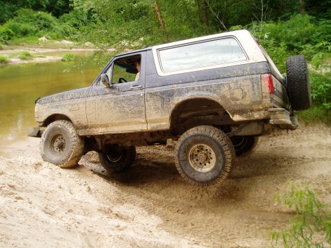 1990 Ford Bronco - This SUV is navigating a challenging off-road terrain with muddy conditions and uneven ground.
