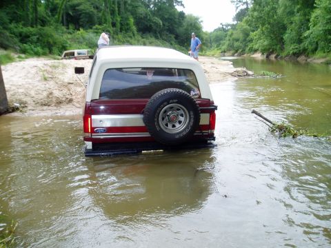 1990 Ford Bronco - A 1990 Ford Bronco navigates a shallow river with another vehicle visible in the background.
