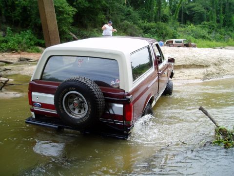 1990 Ford Bronco - Two Ford Broncos navigating a water crossing on a dirt road.