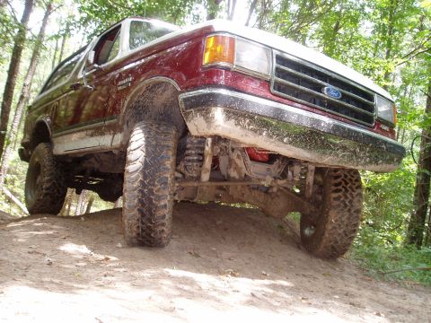 1990 Ford Bronco - Muddy 1990 Ford Bronco climbing a dirt hill with trees in the background.