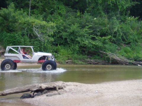 1990 Ford Bronco - Custom buggy navigates a water crossing with a wooded shoreline.