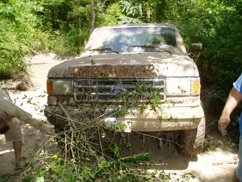 1990 Ford Bronco - A muddy Ford truck is stuck in a ditch, with two people nearby.