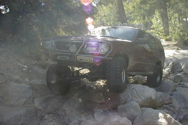 Brown SUV with bull bar and winch climbing over rocks. License plate reads T 104X4