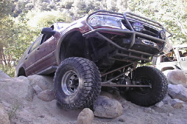 Maroon 1997 Ford Ranger off-roading on rocks, lifted with large tires and custom bumper