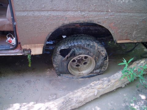 1990 Ford Bronco - Flat tire in mud, likely from off-roading.