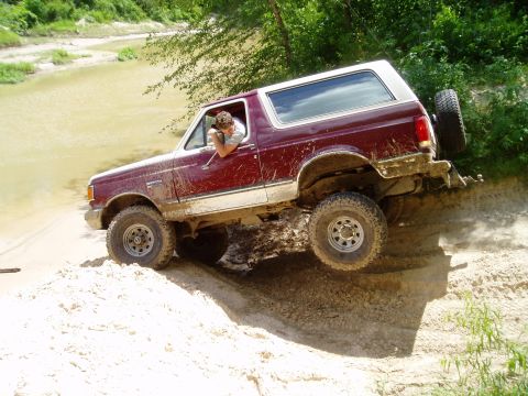 1990 Ford Bronco - This 1990 Ford Bronco is navigating a challenging off-road trail near a body of water.