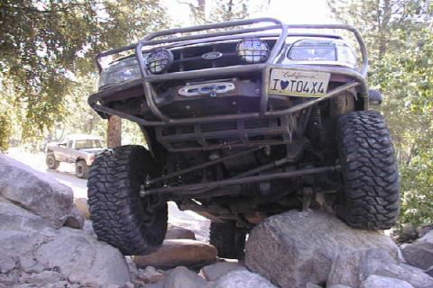 1997 Ford Ranger - A modified red Ford Ranger navigates a rocky trail, with another truck visible in the background.